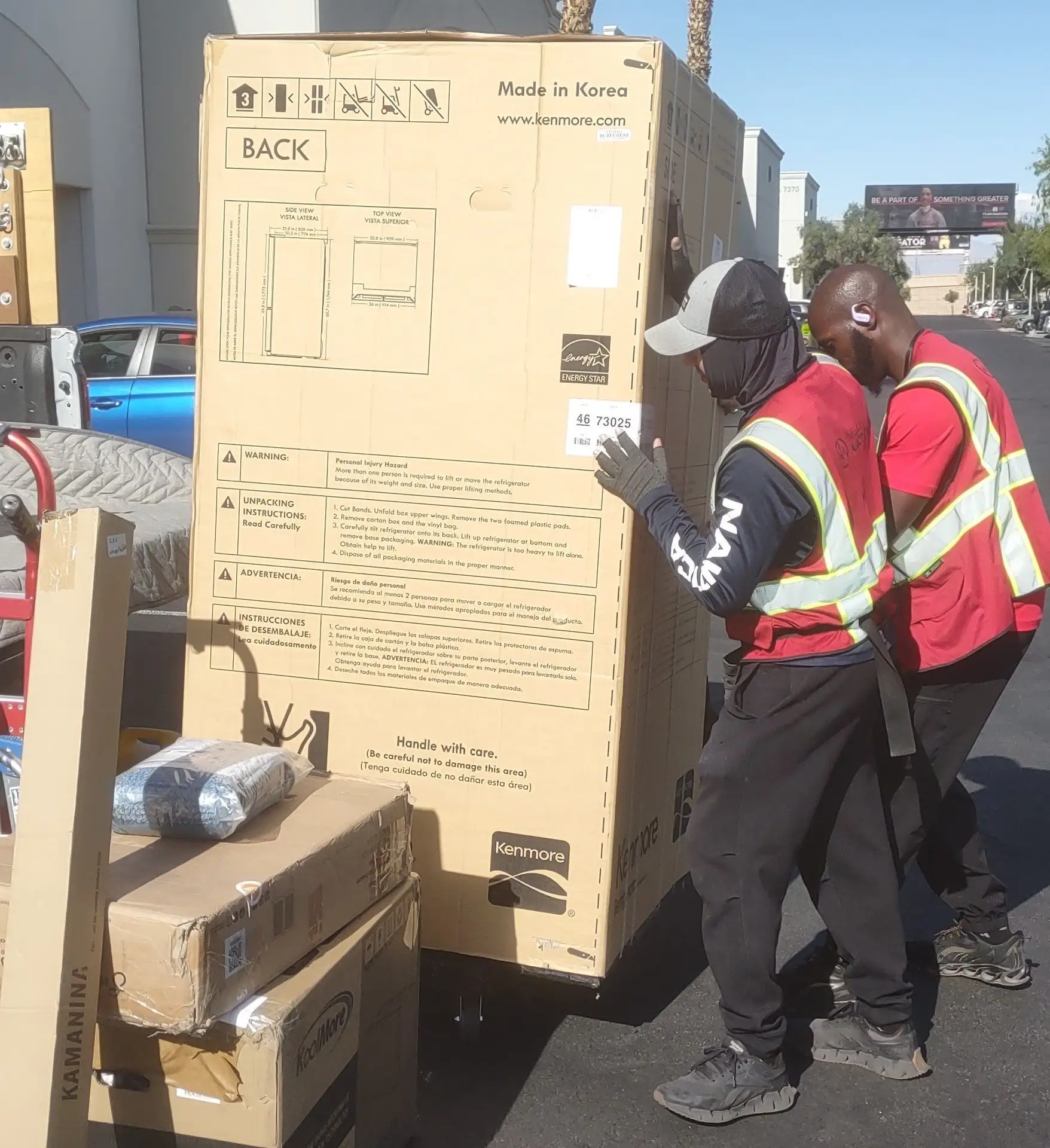 2 men working about for moving help, loading a large refrigerator into the back of a pick up truck with other boxes for furniture assembly.