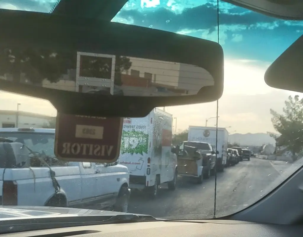 Looking out the windshield of a pick up truck, hired for trash removal services, at a long line waiting to enter the landfill